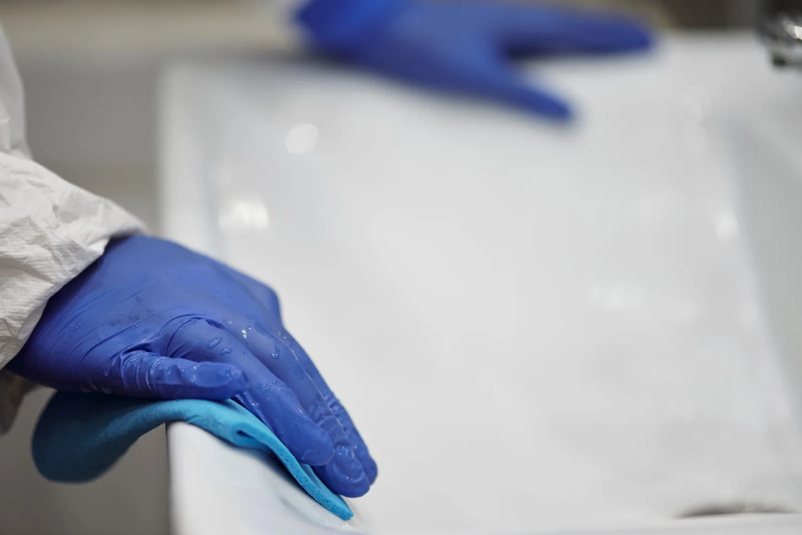 Blue-gloved hands cleaning a white basin